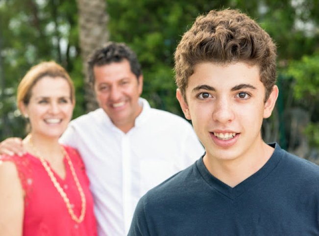 Smiling teenage boy posing with his parents in the background