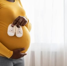 Closeup of baby shoes on pregnant black lady belly